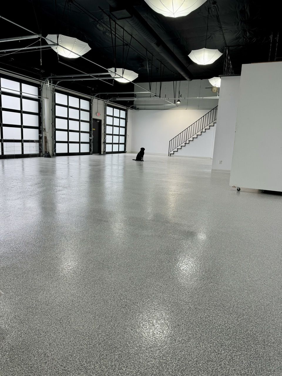 The studio floor with five frosted glass garage doors, hanging umbrella lights and a staircase to the loft